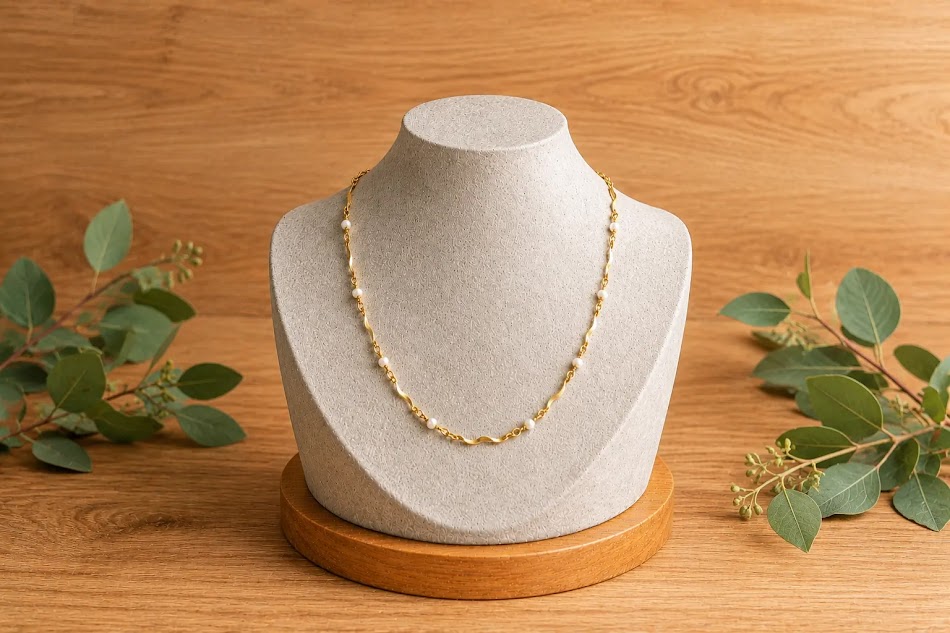 colar perola banhada a ouro 18k, mostruario de cimento , fundo de madeira e folhagens.