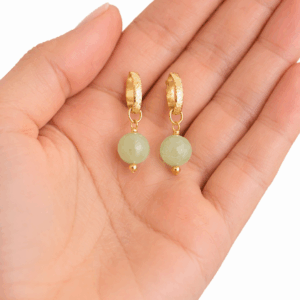 brincos de jade banhados a ouro 18k. na palma da mão da modelo.