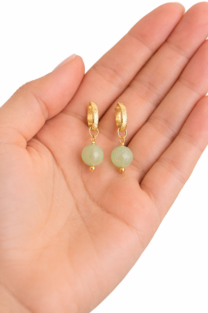 brincos de jade banhados a ouro 18k. na palma da mão da modelo. brincos de jade banhados a ouro 18k. na palma da mão da modelo.