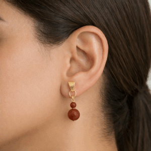 brincos de jaspe vermelho banhado a ouro 18k. no lobulo da modelo