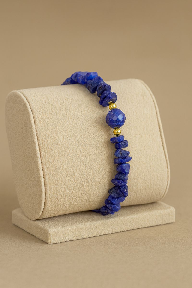 Pulseira de lápis-lazúli exibida em mostruário bege de joalheria, com cascalhos irregulares e detalhes folheados a ouro 18k” Pulseira de lápis-lazúli exibida em mostruário bege de joalheria, com cascalhos irregulares e detalhes folheados a ouro 18k”
