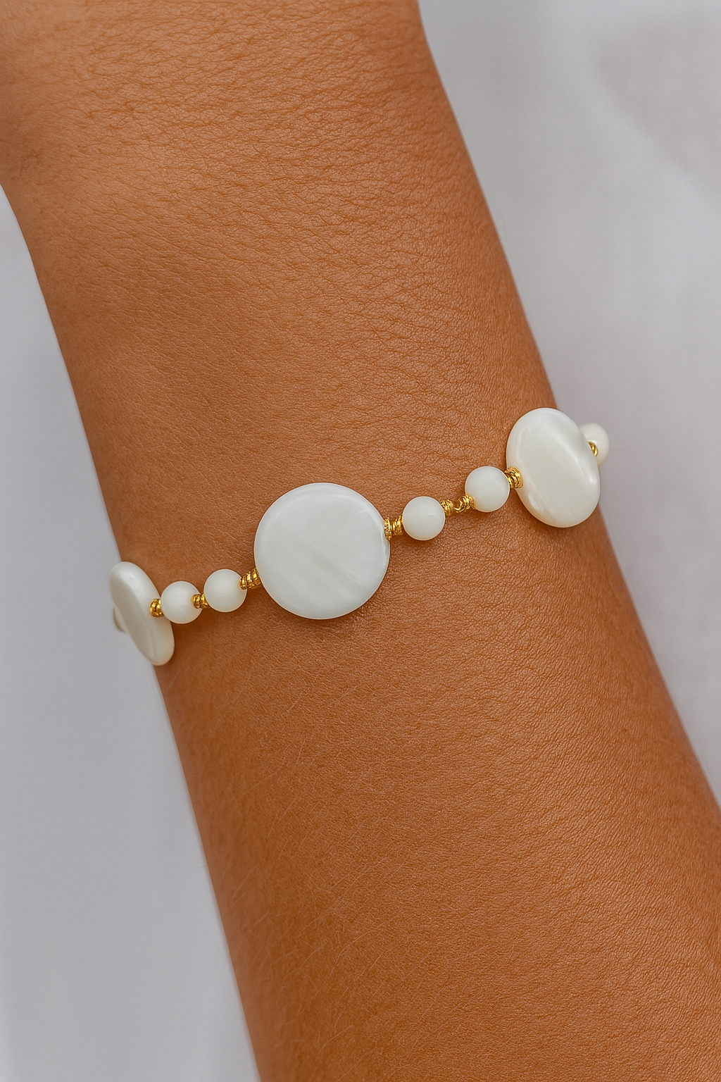 pulseira artesanal de madrepérola com esferas e bolachinhas intercaladas por entremeios banhados a ouro 18k no pulso feminino – biojoia exclusiva Ceci Joias da Amazônia.