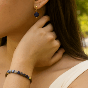 Modelo feminina de 25 anos usando brincos de sodalita e pulseira de sodalita e madeira de sândalo folheados a ouro 18k, em close com luz natural do dia, joias artesanais da Ceci Joias da Amazônia.