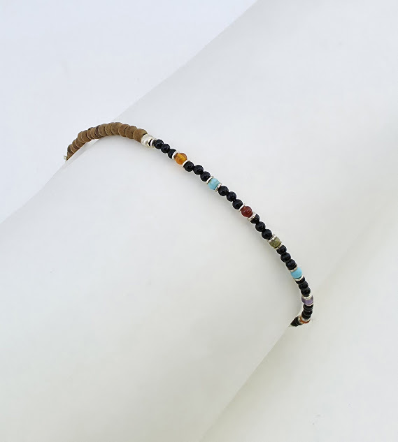 pulseira artesanal de ônix e pedras brasileiras coloridas de 2 mm com contas de sândalo, disposta sobre rolo branco de exposição, joia delicada e minimalista pulseira artesanal de ônix e pedras brasileiras coloridas de 2 mm com contas de sândalo, disposta sobre rolo branco de exposição, joia delicada e minimalista
