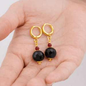 Brincos artesanais de turmalina negra e rubi folheados a ouro 18k sobre a mão da modelo