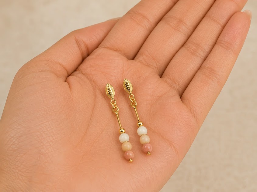 Brincos pendentes de aventurina pêssego com ouro 18k, exibidos na palma da mão, mostrando as esferas polidas de 4mm e o acabamento banhado em ouro Brincos pendentes de aventurina pêssego com ouro 18k, exibidos na palma da mão, mostrando as esferas polidas de 4mm e o acabamento banhado em ouro